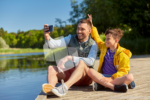 Image of father and son taking selfie with phone on river