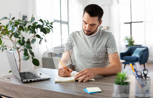 Image of man with notebook and laptop at home office