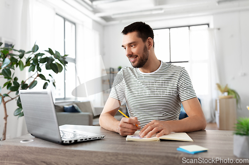 Image of man with notebook and laptop at home office