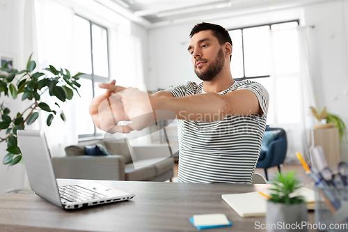Image of man with laptop stretching at home office