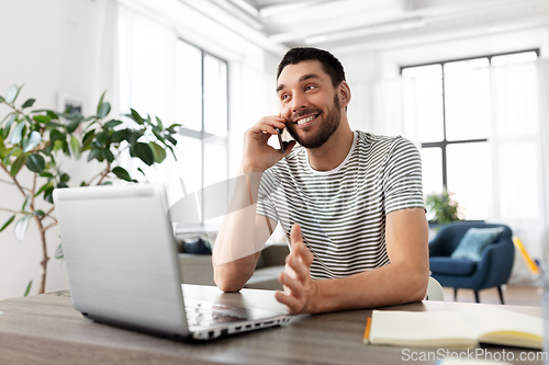 Image of man with laptop calling on phone at home office