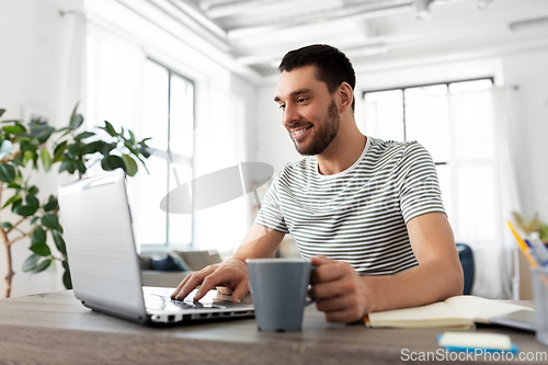 Image of man with laptop drinking coffee at home office