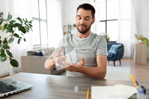 Image of man using hand sanitizer at home office