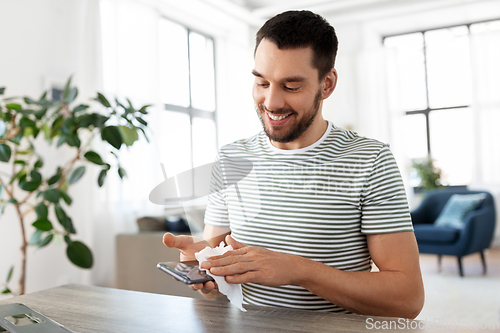 Image of man cleaning phone with wet wipe at home office