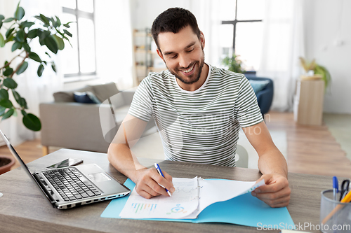 Image of man with papers and laptop working at home office