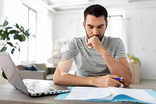 Image of man with papers and laptop working at home office