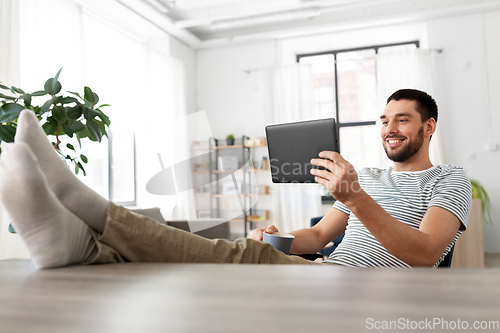 Image of man with tablet pc resting feet on table at home