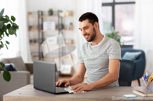 Image of man cleaning laptop with wet wipe at home office