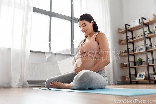 Image of happy pregnant woman sitting on yoga mat at home