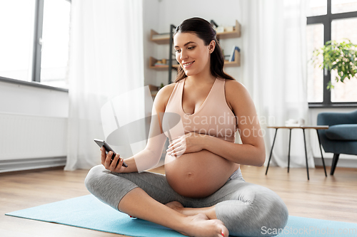 Image of happy pregnant woman with phone doing yoga at home