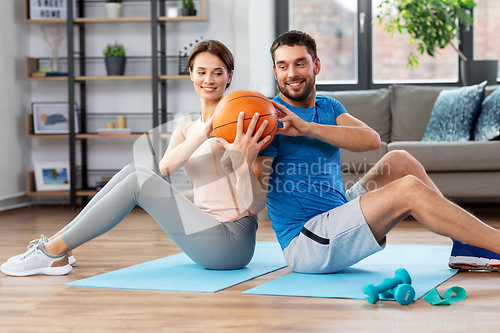 Image of happy couple exercising with ball at home