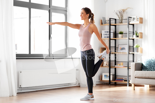 Image of smiling young woman stretching leg at home