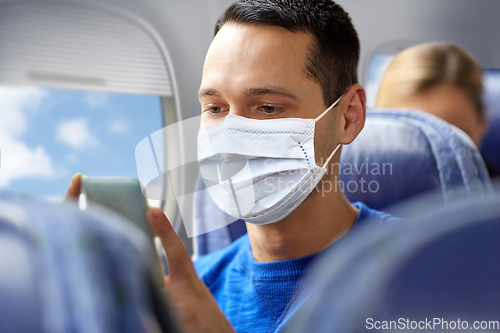 Image of man in mask sitting in plane with smartphone