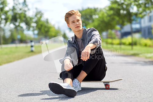Image of teenage boy sitting on skateboard on city street