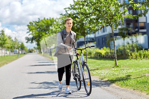 Image of young man with bicycle walking along city street