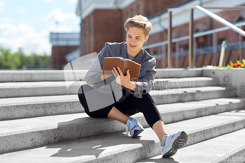 Image of young man or teenage boy reading book in city