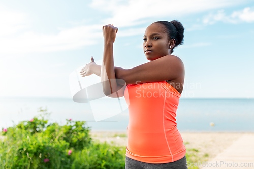 Image of young african american woman stretching on beach