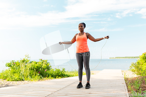 Image of african woman exercising with jump rope on beach