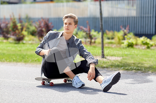 Image of teenage boy sitting on skateboard on city street