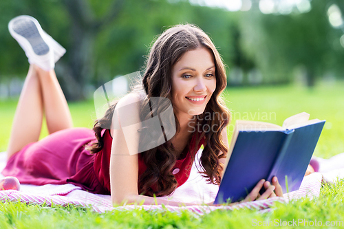 Image of happy smiling woman reading book at summer park