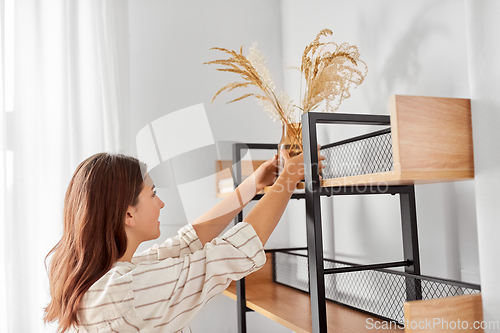 Image of woman decorating home with dried flowers in vase