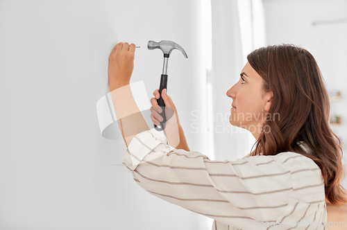 Image of woman hammering nail to wall at home