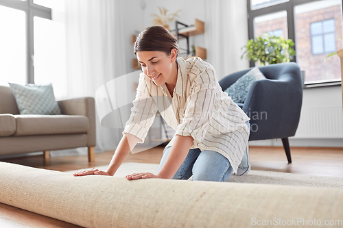 Image of young woman unfolding carpet at home