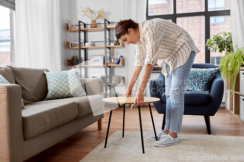 Image of woman placing coffee table next to sofa at home