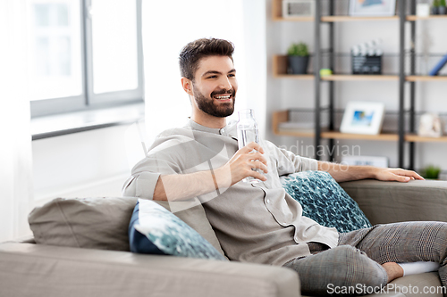 Image of happy man drinking water from glass bottle at home