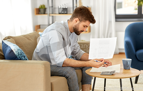 Image of man with bills counting on calculator at home