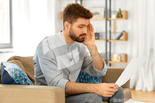 Image of unhappy man with bills or tax report at home