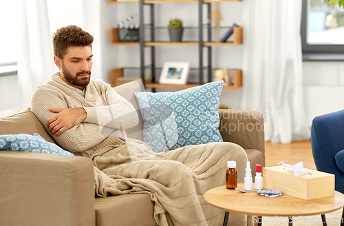 Image of sad sick man in blanket with medicine at home