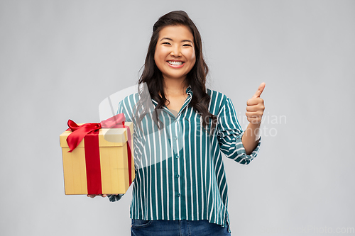 Image of happy asian woman with gift box showing thumbs up