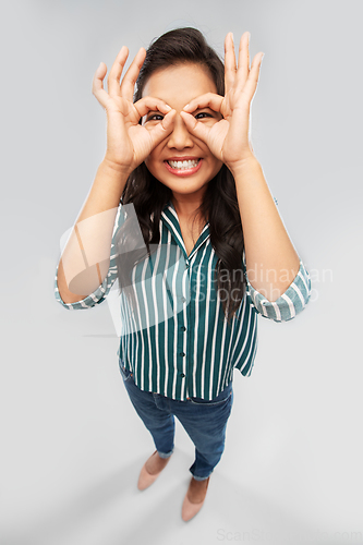 Image of smiling asian woman looking through finger glasses