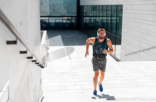 Image of young man in headphones running upstairs outdoors