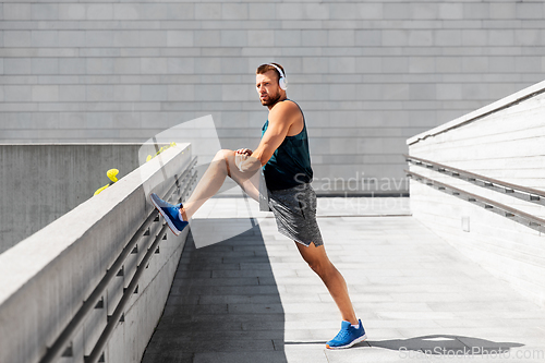Image of young man in headphones stretching leg outdoors