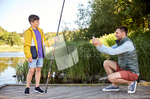 Image of father photographing son with fishing rod on river