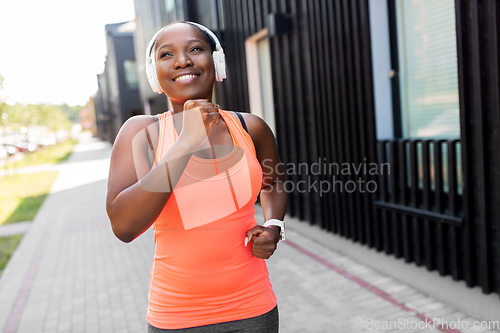 Image of happy african woman in headphones running outdoors