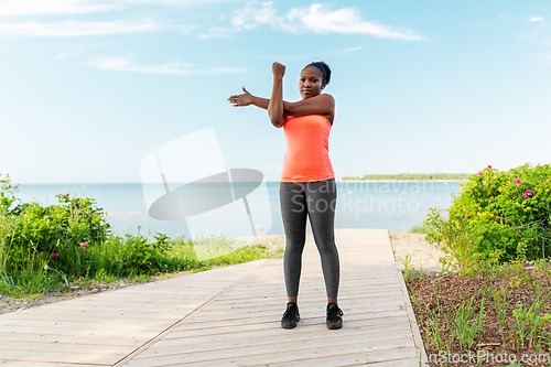 Image of young african american woman stretching on beach