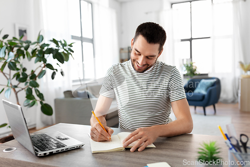 Image of man with notebook and laptop at home office