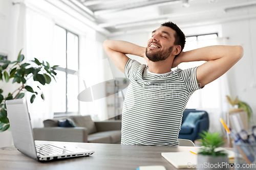 Image of happy man with laptop stretching at home office