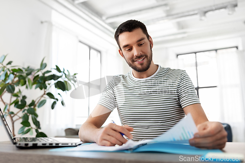 Image of man with papers and laptop working at home office