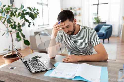 Image of man with papers and laptop working at home office