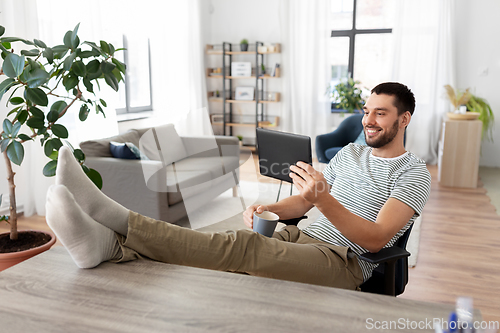 Image of man with tablet pc resting feet on table at home