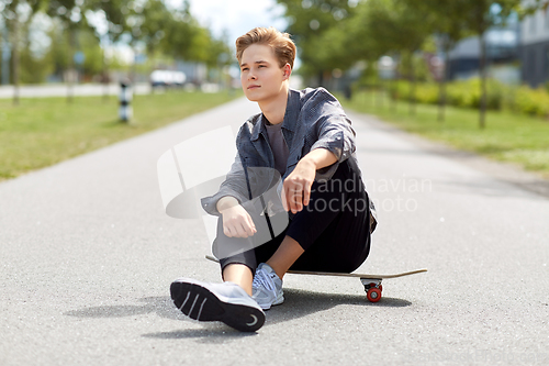 Image of teenage boy sitting on skateboard on city street