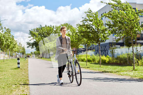 Image of young man with bicycle walking along city street