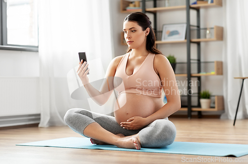 Image of pregnant woman with smartphone exercising at home