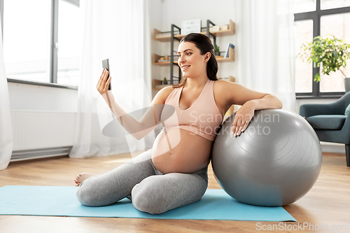 Image of pregnant woman with smartphone and fitball at home