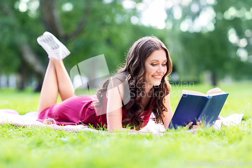 Image of happy smiling woman reading book at summer park
