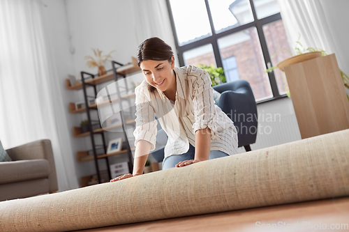 Image of young woman unfolding carpet at home